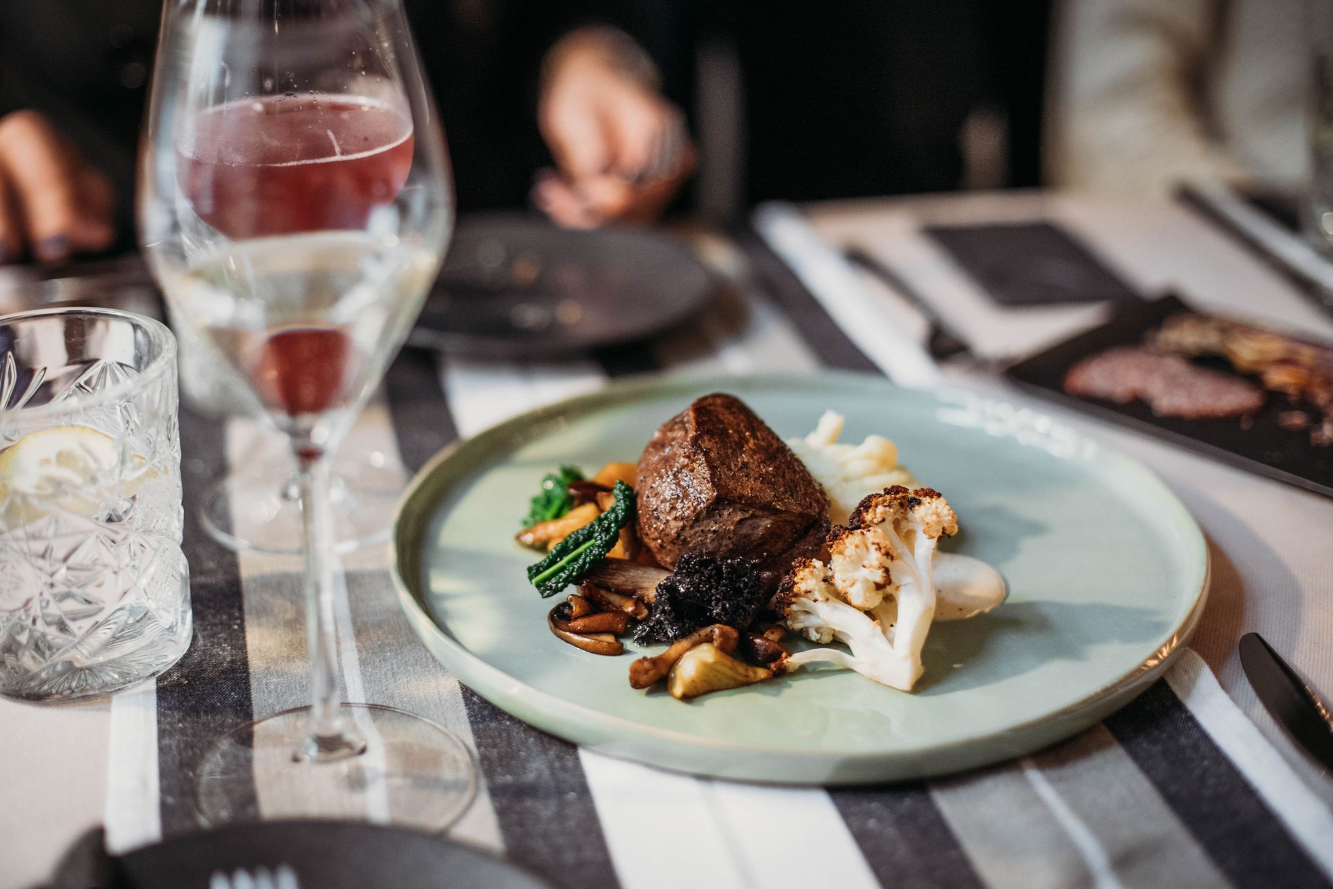 Tasty grilled steak served with cauliflower and mushrooms placed on table with wineglass filled with