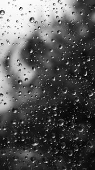 Black and white image of raindrops on a window, creating a moody and textured effect.