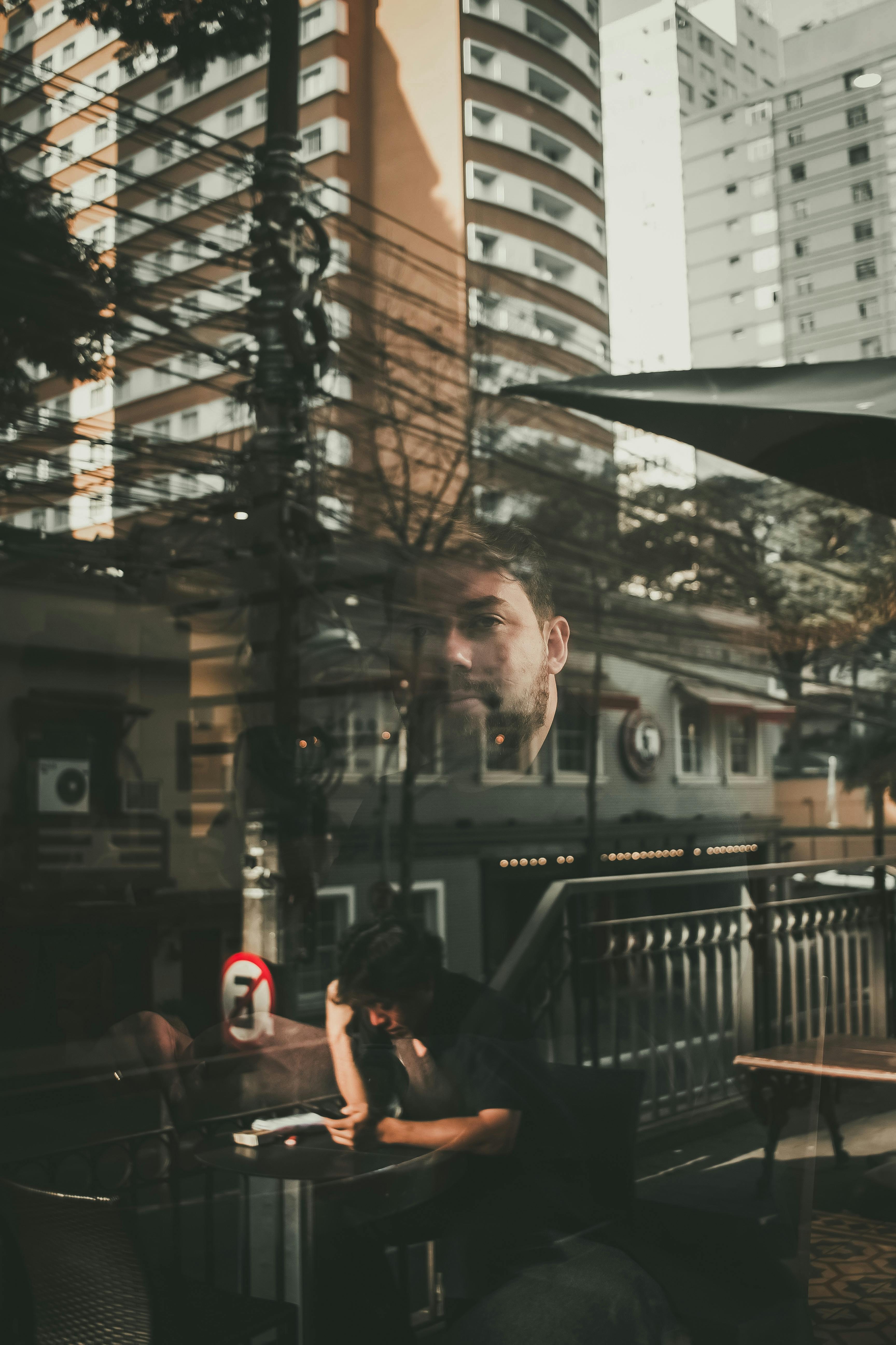 man chatting on smartphone at cafe table against glass wall