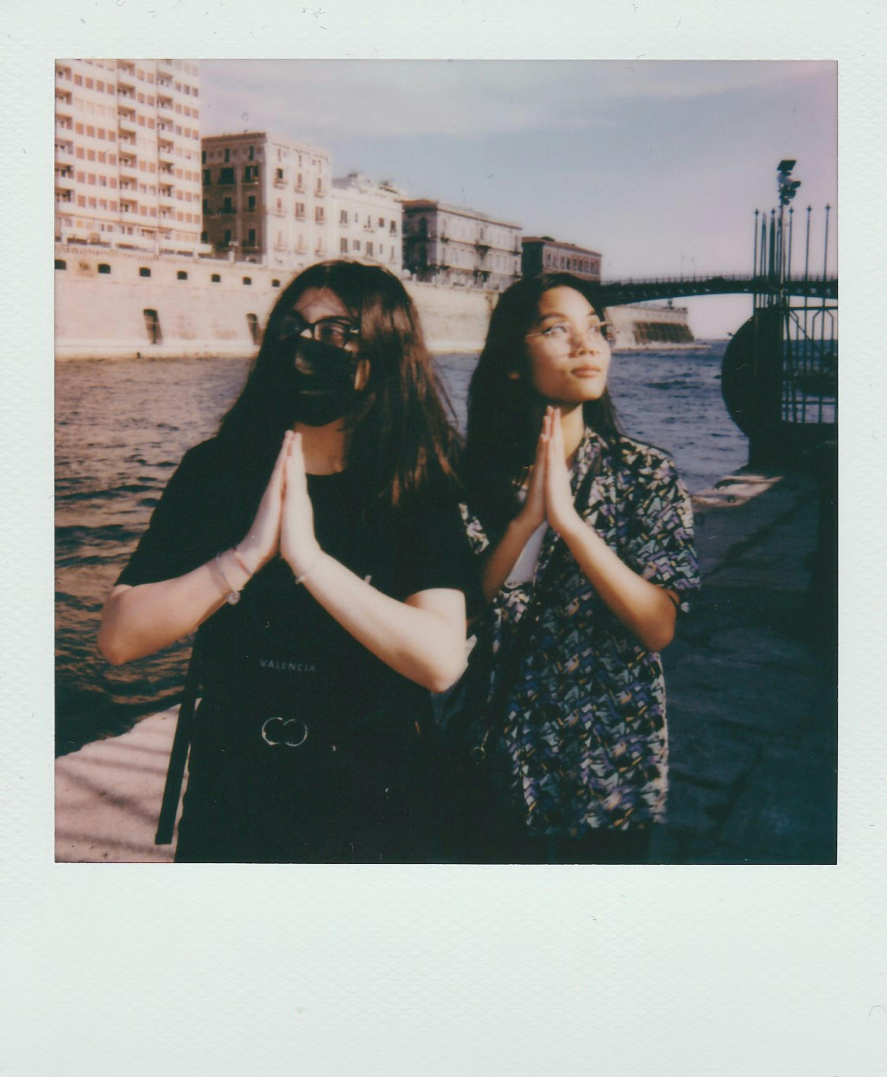 Two women in prayer pose by the waterfront in Taranto, Italy.