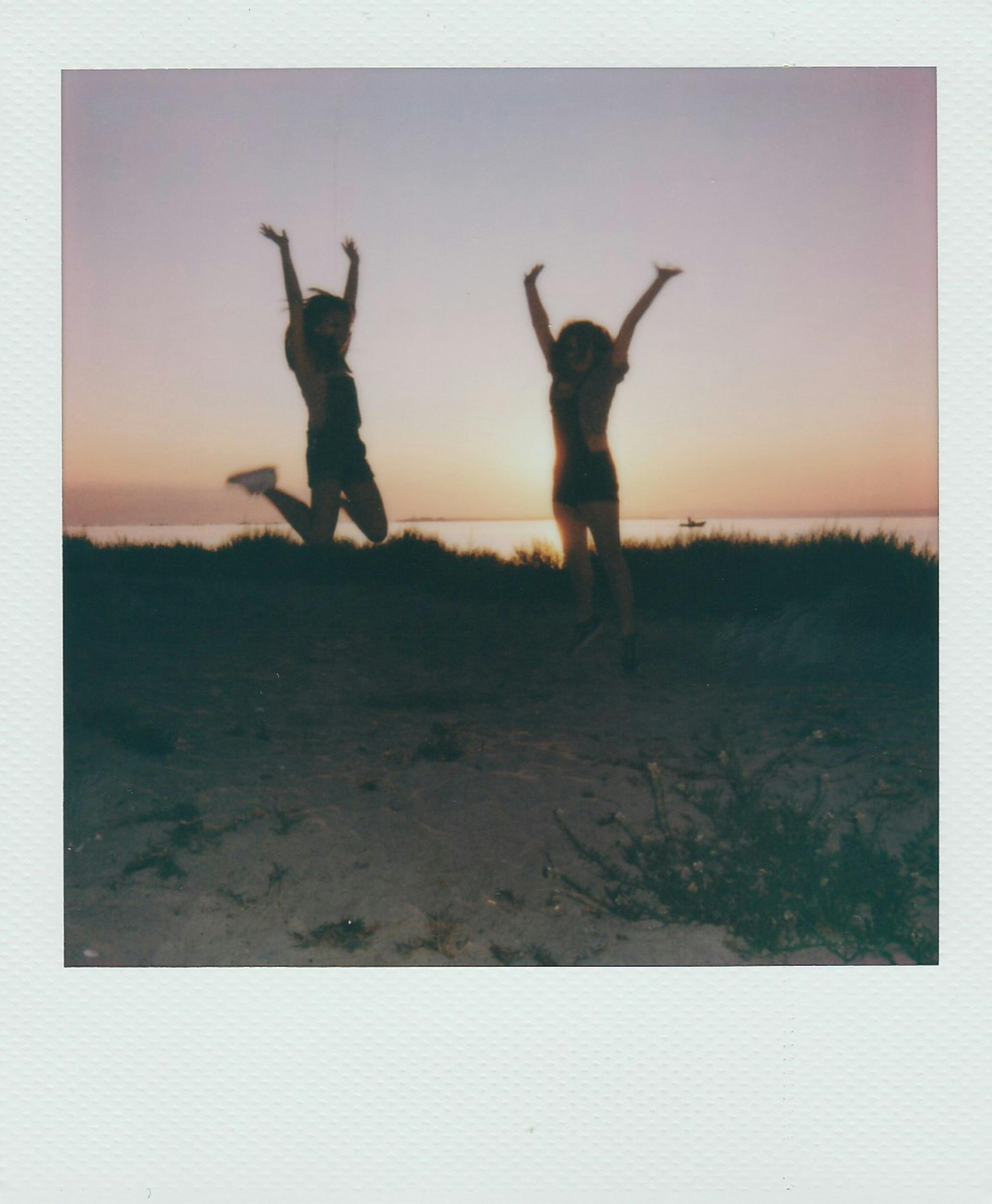 Silhouettes of women jumping with joy at sunset on a beach in Taranto, Italy.