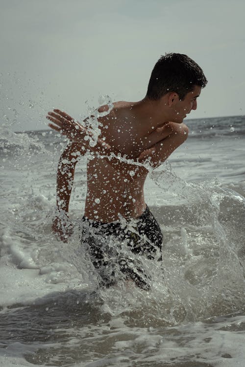 Photo of Shirtless Man Splashing Water at the Beach