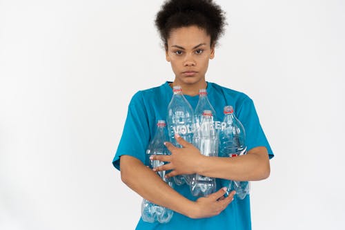 An Afro-Haired Woman in Blue Shirt Holding Plastic Bottles