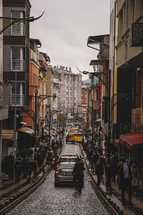 Free A busy city street scene featuring colorful buildings, vehicles, and pedestrians on a cloudy day. Stock Photo