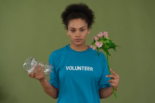 Free A Woman in Blue Shirt Holding Plastic and Flowers Stock Photo