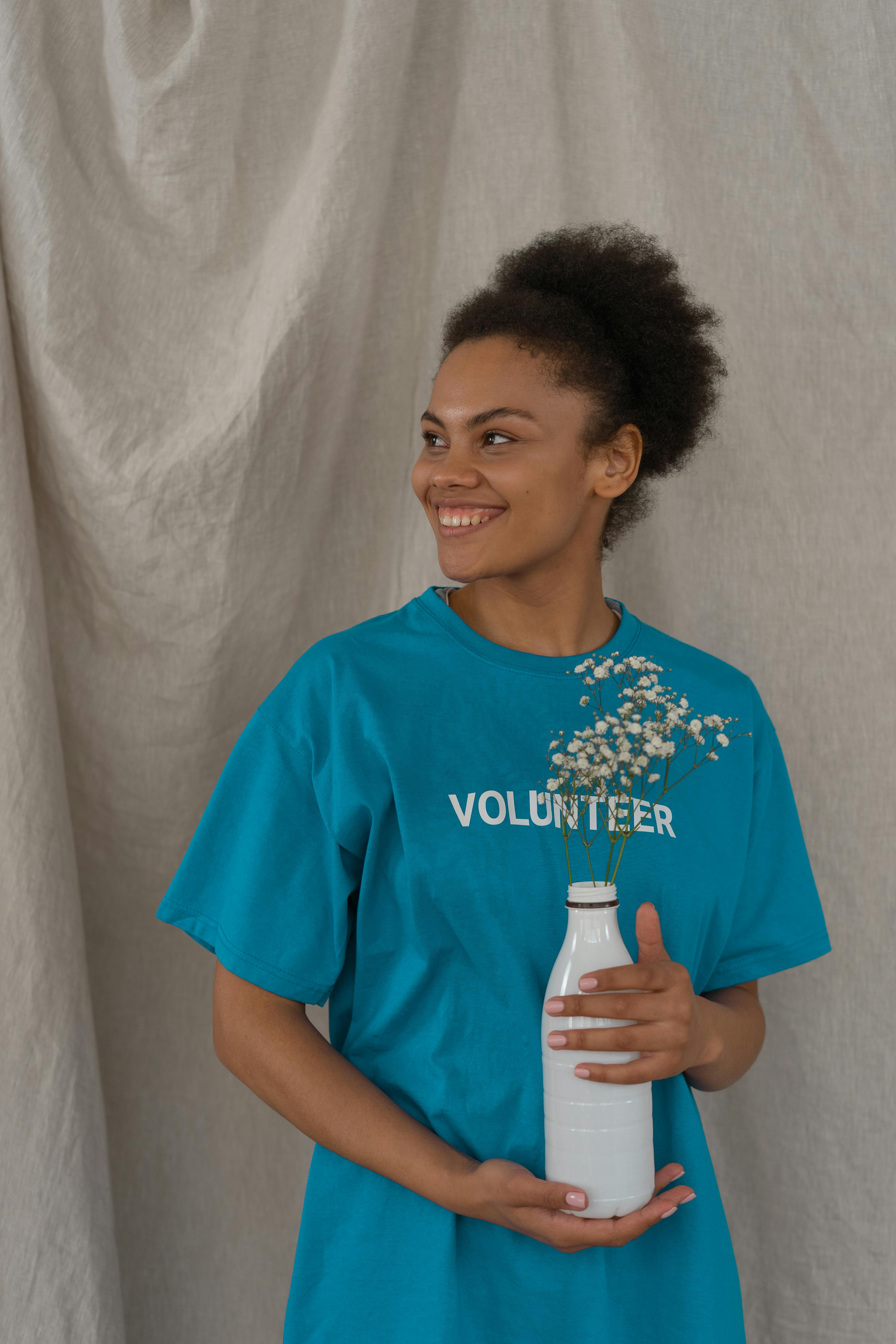 A cheerful woman in a volunteer shirt holding a bottle with flowers.