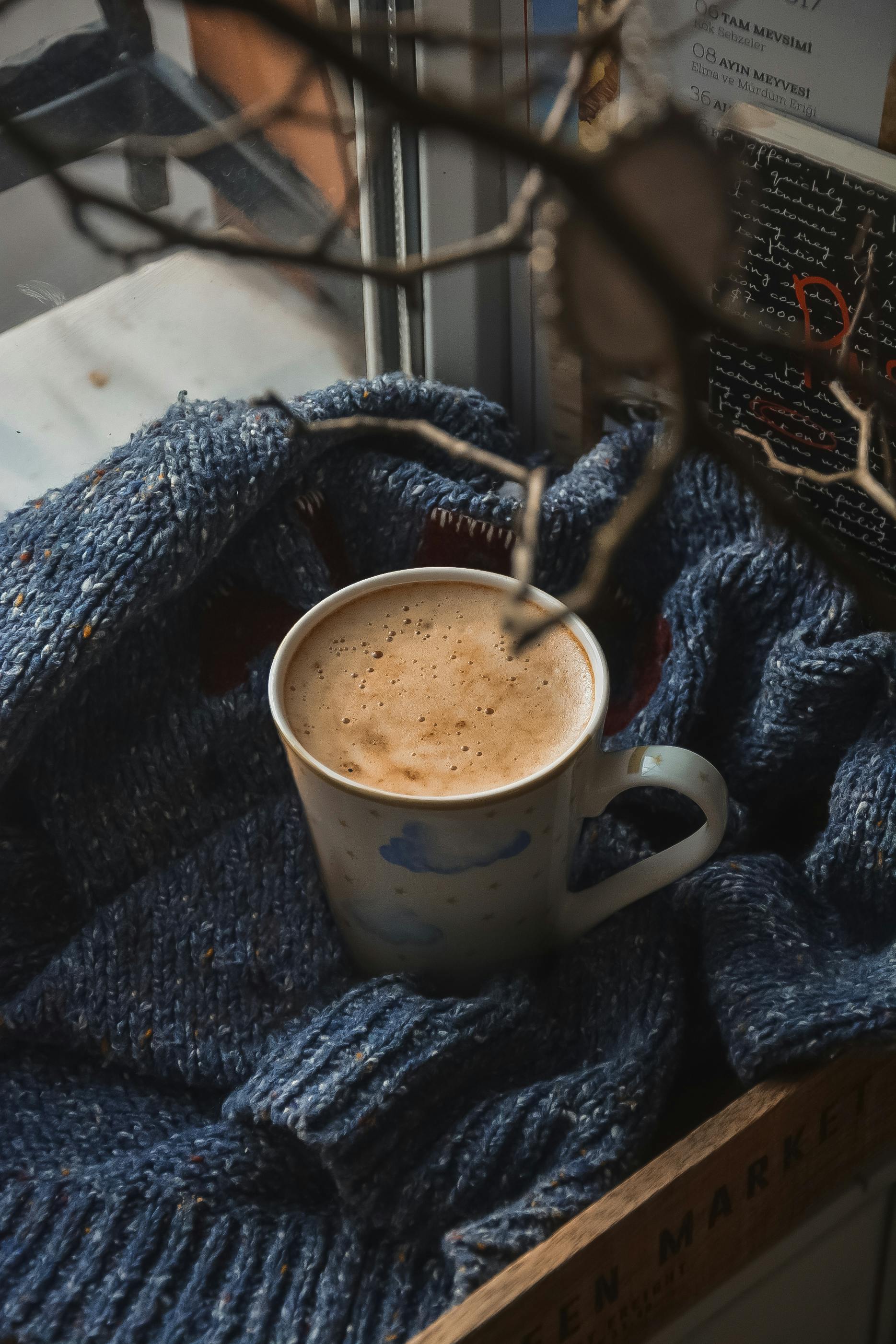 Free Warm coffee cup nestled in a blue knitted blanket by the window, creating a cozy atmosphere. Stock Photo