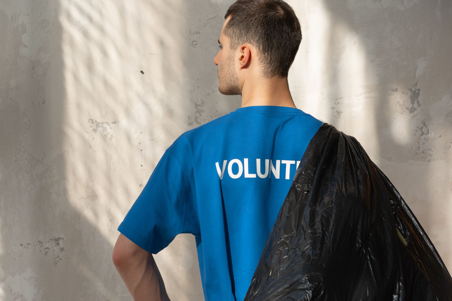 Man in blue volunteer shirt holding garbage bag, symbolizing environmental conservation and cleanup efforts.