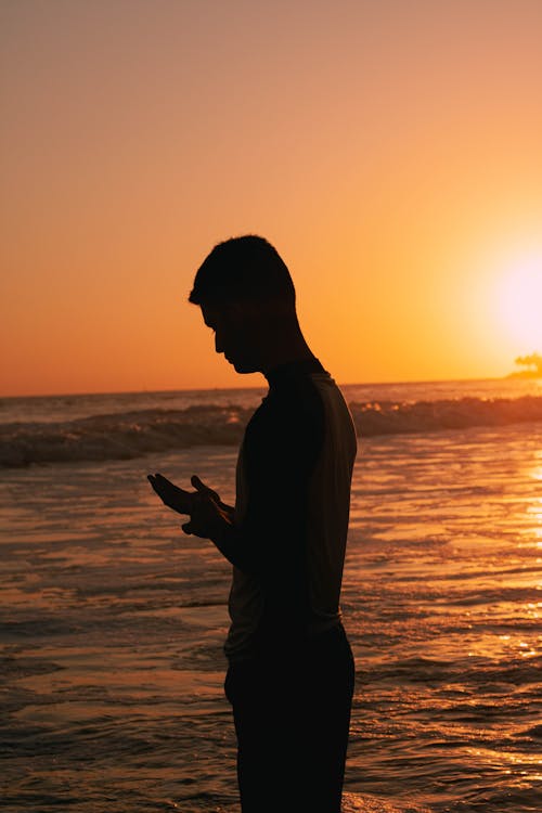 Silhouette of a Person Standing on the Beach during Sunset