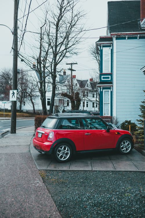 Free Red car parked in pavement road near building and leafless trees in residential district in city in autumn time in daylight Stock Photo