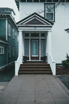Facade of contemporary residential house trimmed with white siding with brown stairs and glass door