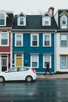 Range of residential houses trimmed with colorful wooden panels in cloudy day on street with parked white car and pedestrian walking on sidewalk