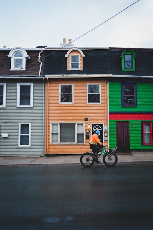 Bicyclist riding on asphalt roadside near multicolored building with attic and pavement in city