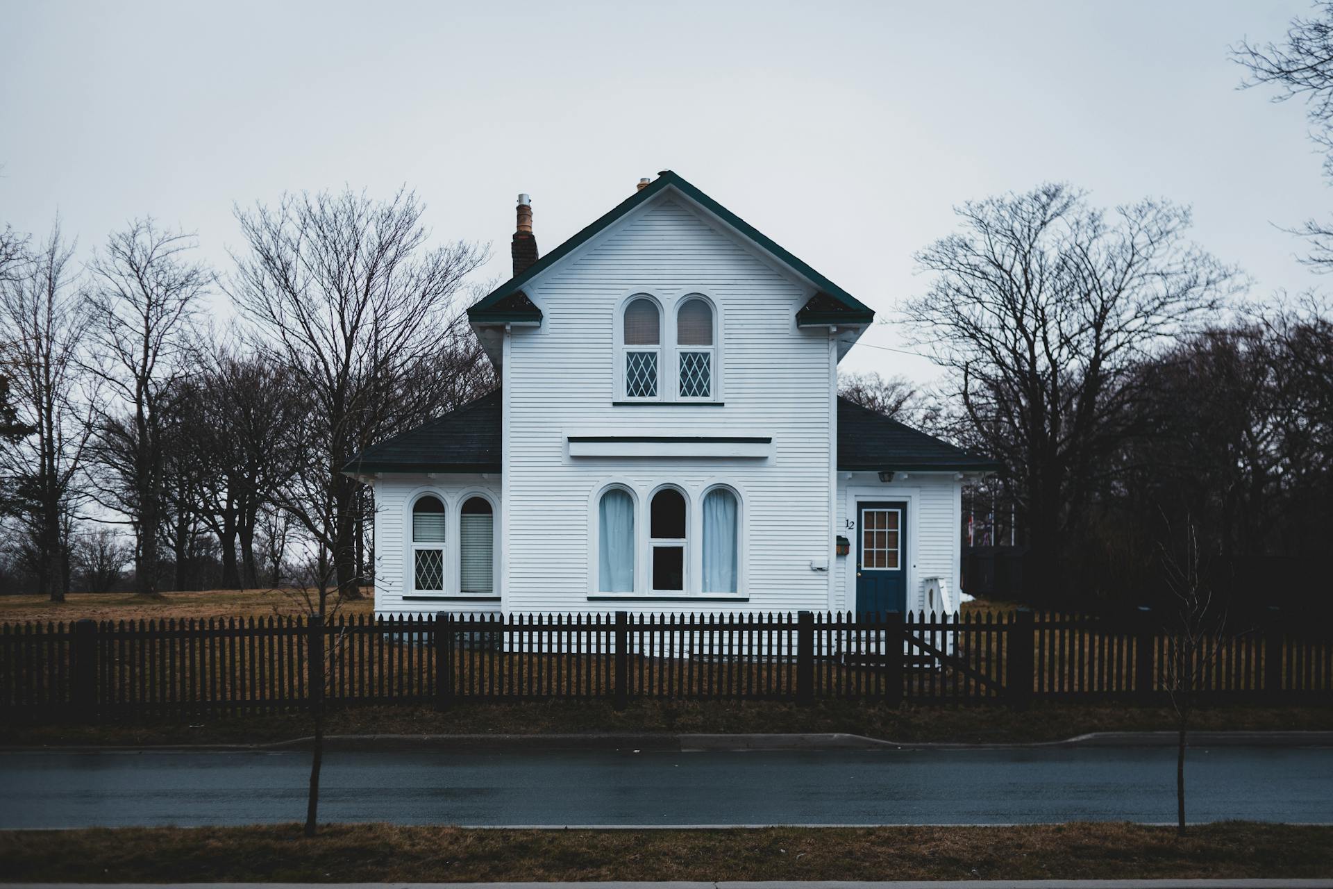 A quaint white cottage house with Gothic windows and picket fence in a suburban fall landscape.