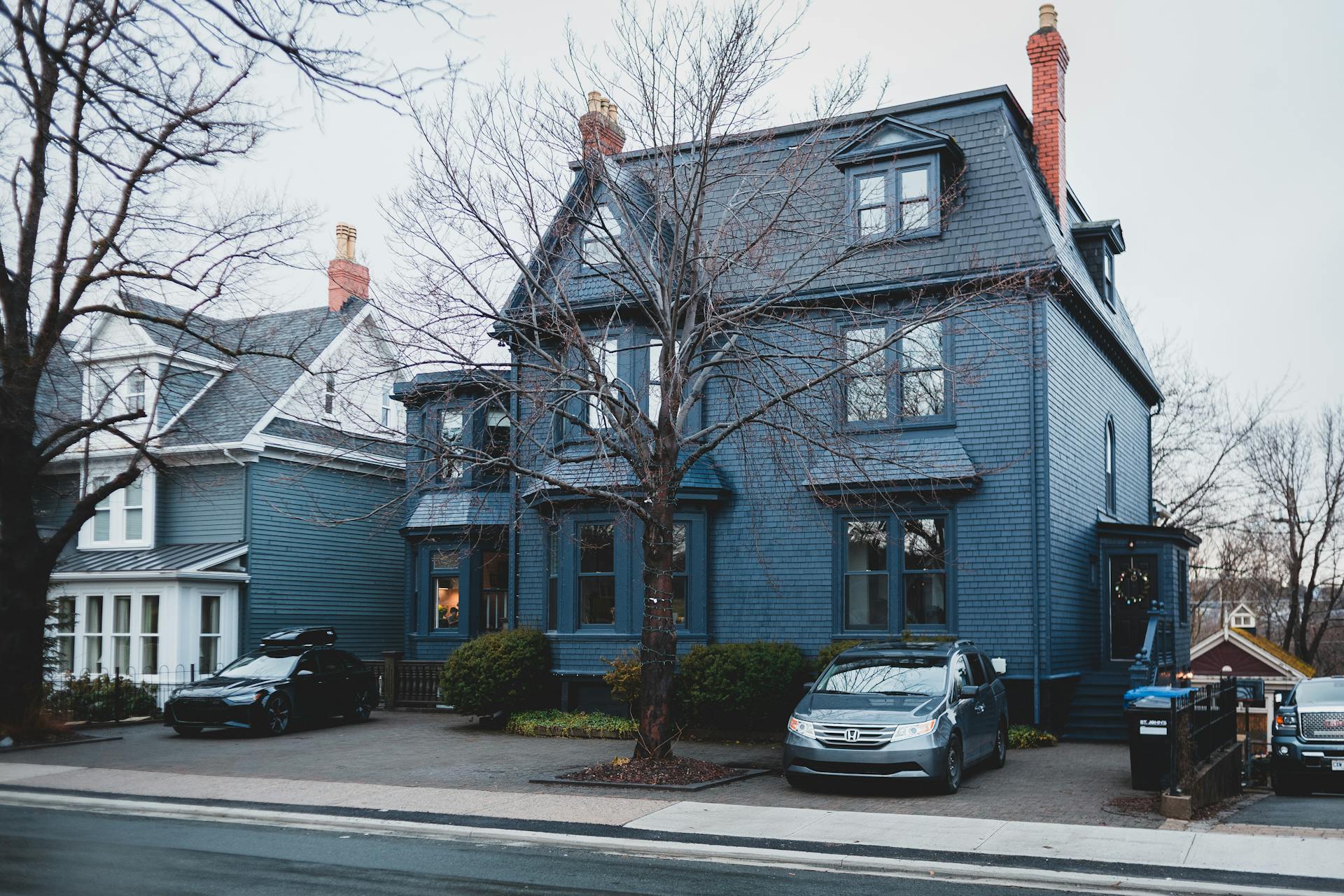 A picturesque Victorian home in a suburban neighborhood during autumn. Parked cars line the street.