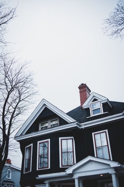 From below of residential building facade with windows and chimney near attics on roof under gloomy sky