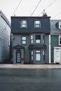 Exterior of aged residential house trimmed with gray wooden panels with glass door and post box on wall in cloudy day
