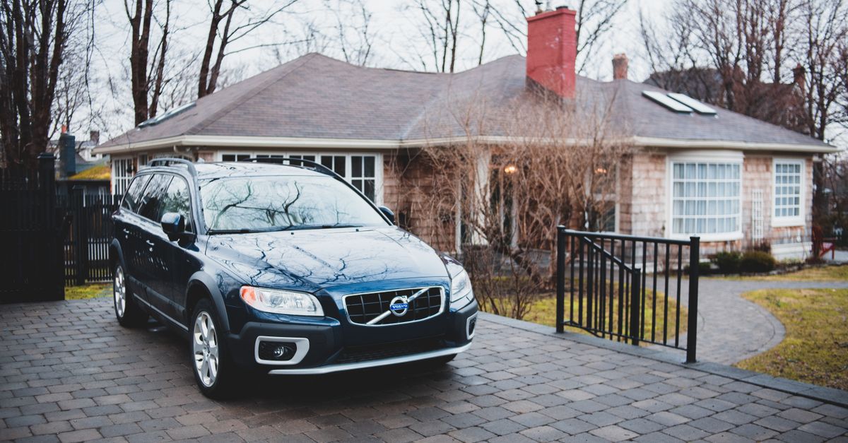 Exterior of new dark blue car placed near brick cottage surrounded by trees in cloudy day