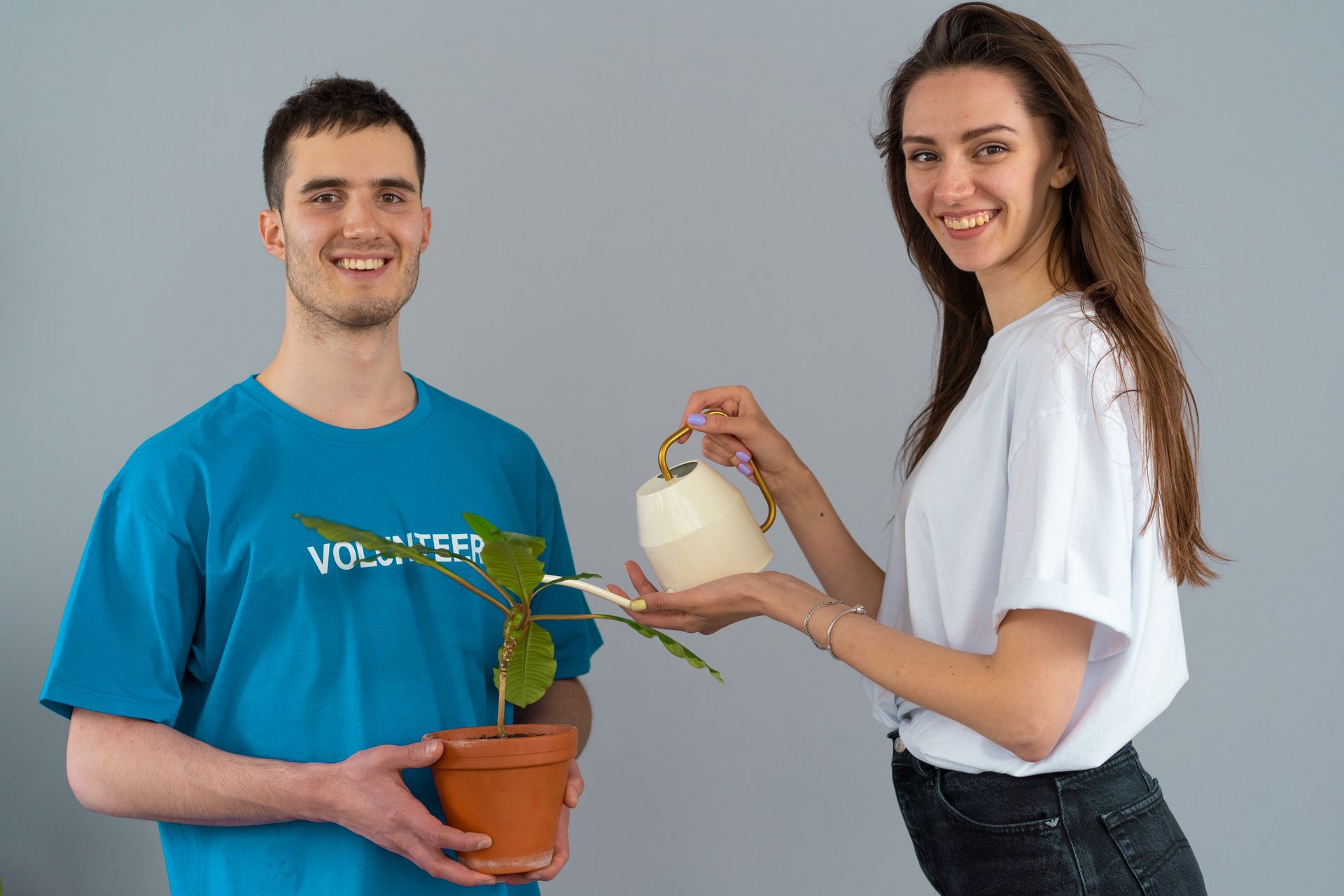 Two volunteers smiling while caring for a potted plant indoors, promoting teamwork and environmental care.