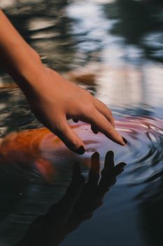 A hand gently touches the rippling water surface in a serene outdoor scene.