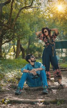 Stylish couple in trendy outfits posing confidently in a sunlit park setting.