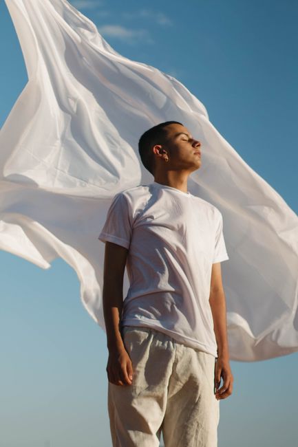 Serene moment with a man outdoors as white fabric flows in the breeze under a clear blue sky.