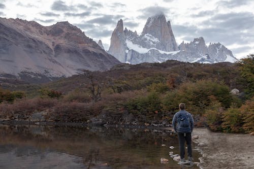 Man in Blue Denim Jacket Standing on a Rock on Lake