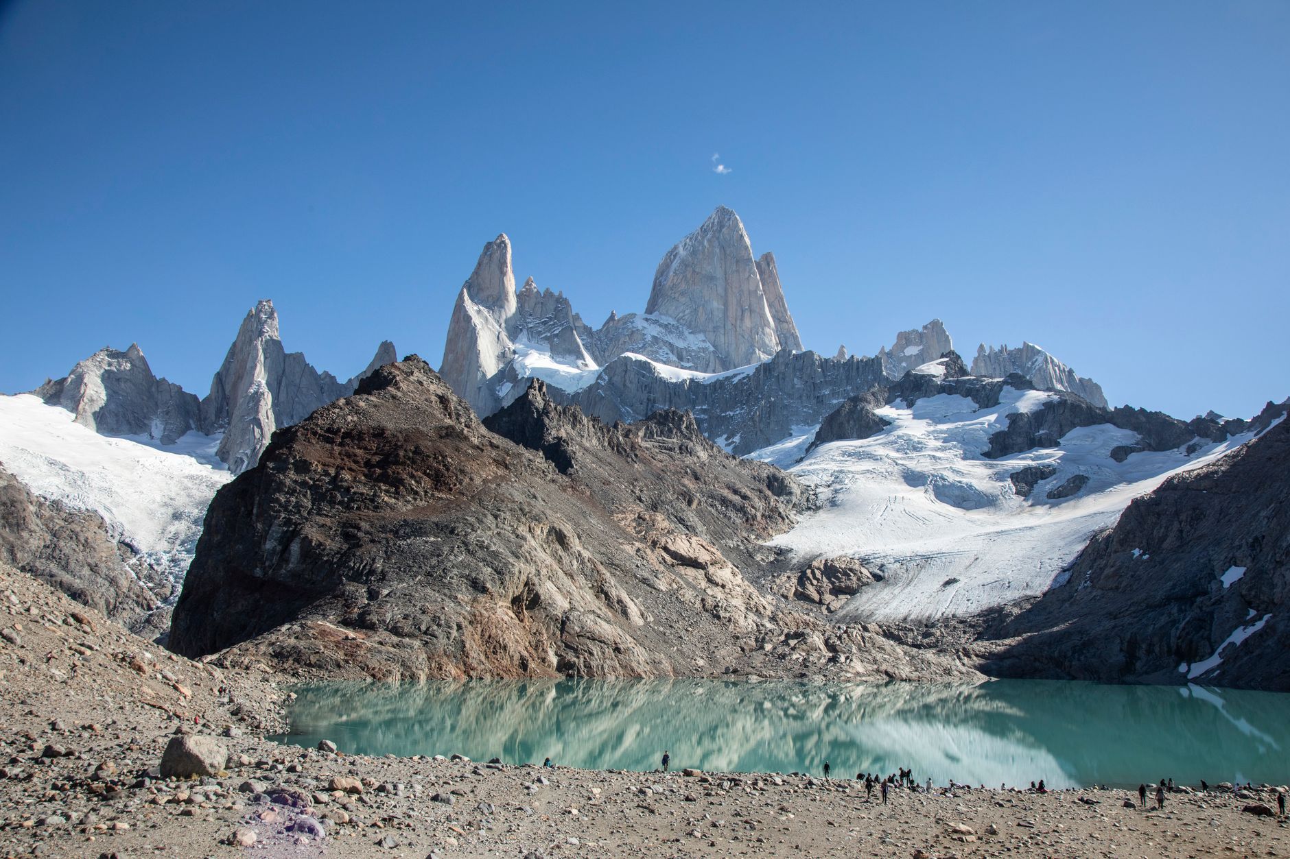 The turquoise glacial lake of Laguna de los Tres at the foot of Mount Fitz Roy, with the granite towers rising above and tiny hikers along the shoreline