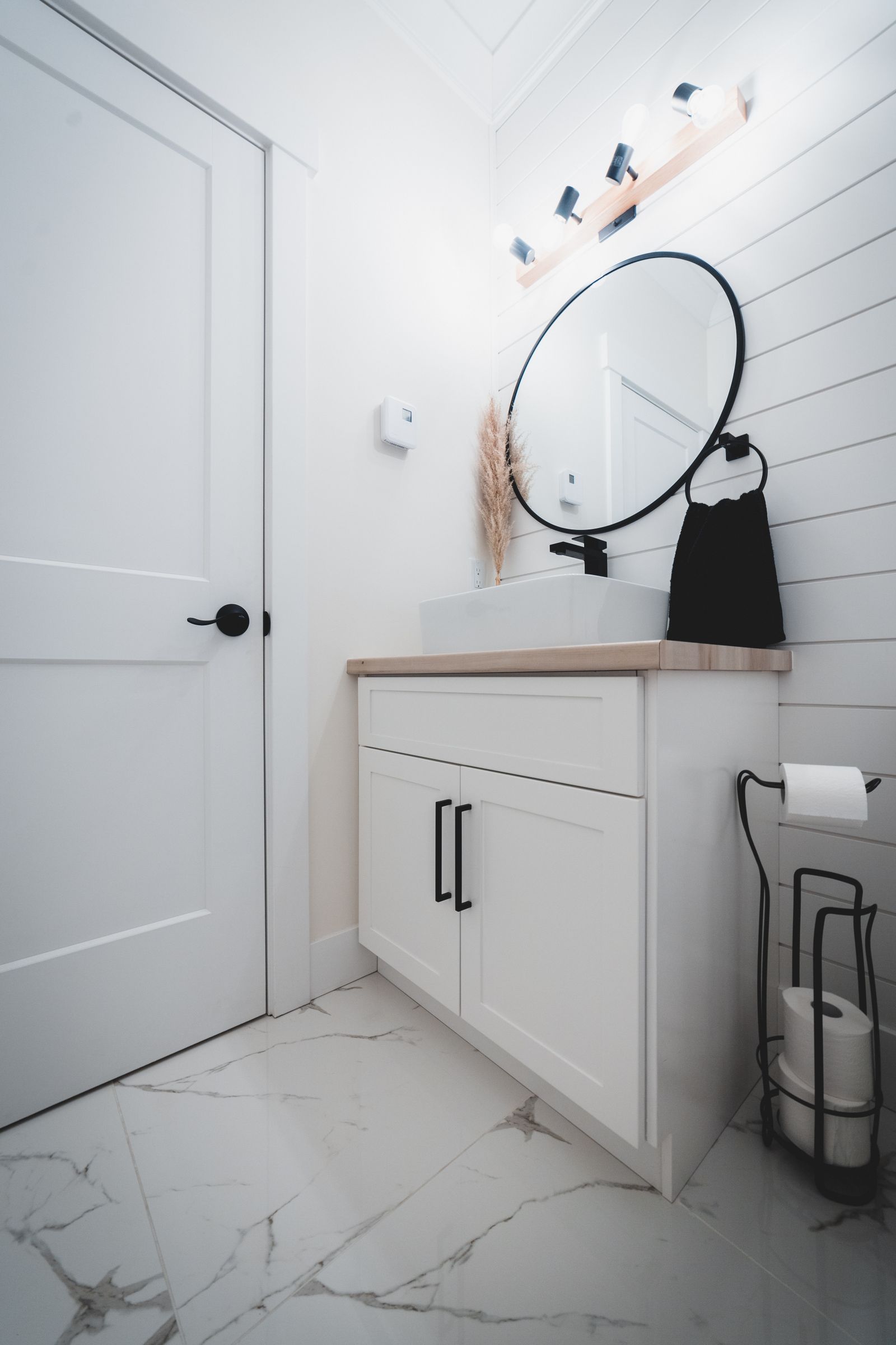 Bright bathroom with a compact white vanity cabinet and round wall mirror; exact cabinet depth is not documented.