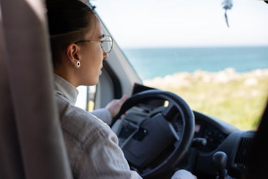 Woman driving a van with ocean backdrop, showcasing a scenic road trip in Portugal.