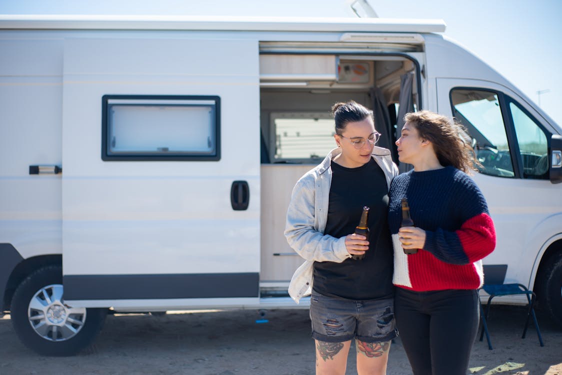 Couple Standing in front of a Campervan and Holding Bottles of Beer 