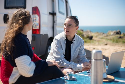 Free Two women relax by their campervan at the Portuguese coast, showcasing love and adventure. Stock Photo