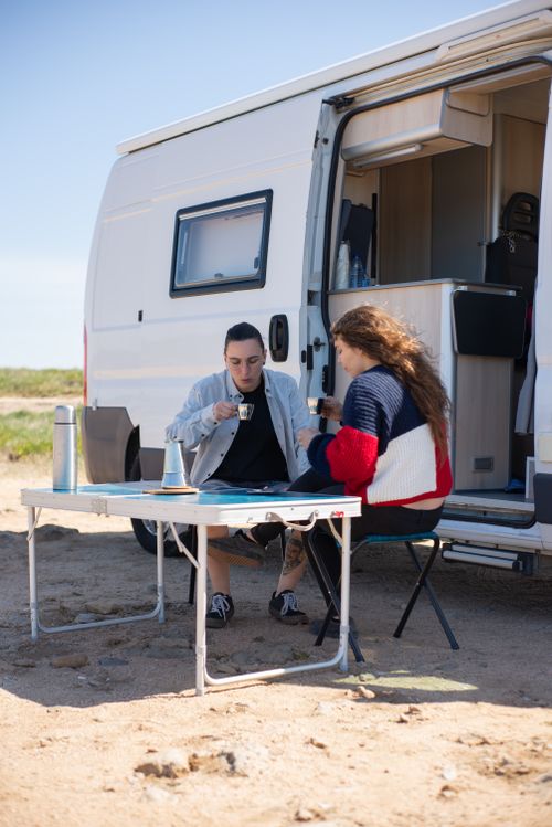 Free Two adults enjoying coffee by a campervan on a sunny beach in Portugal. Stock Photo