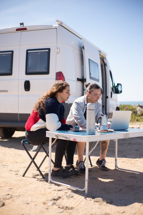 Free A couple enjoying remote work on a laptop while traveling in a camper van with an ocean view in Portugal. Stock Photo