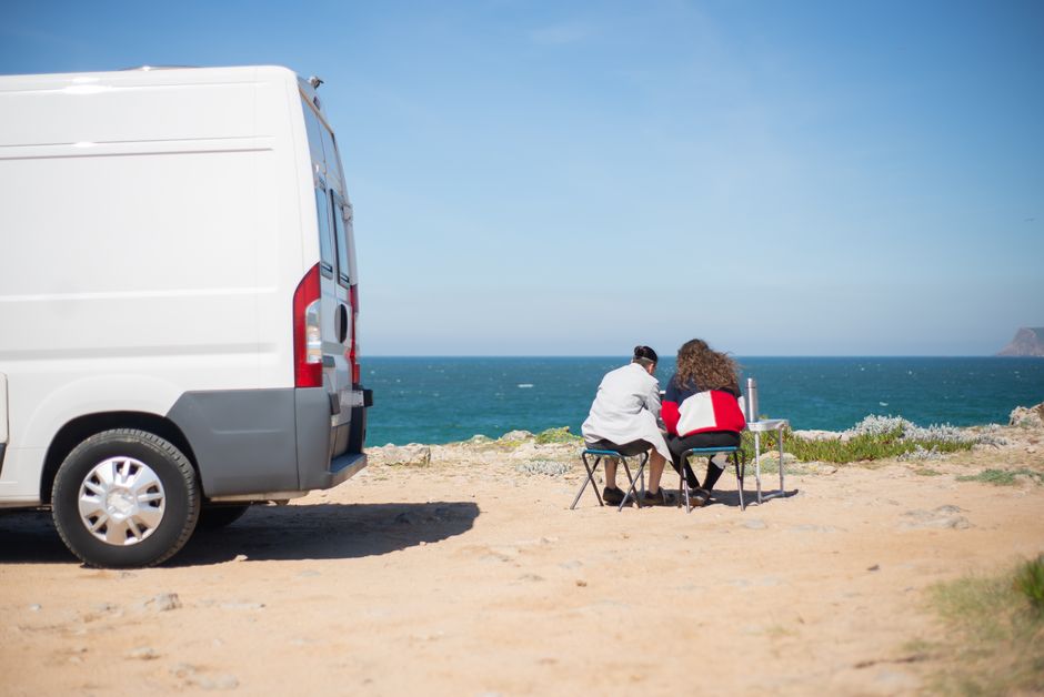 Camper aan een rotskust met twee mensen op klapstoeltjes