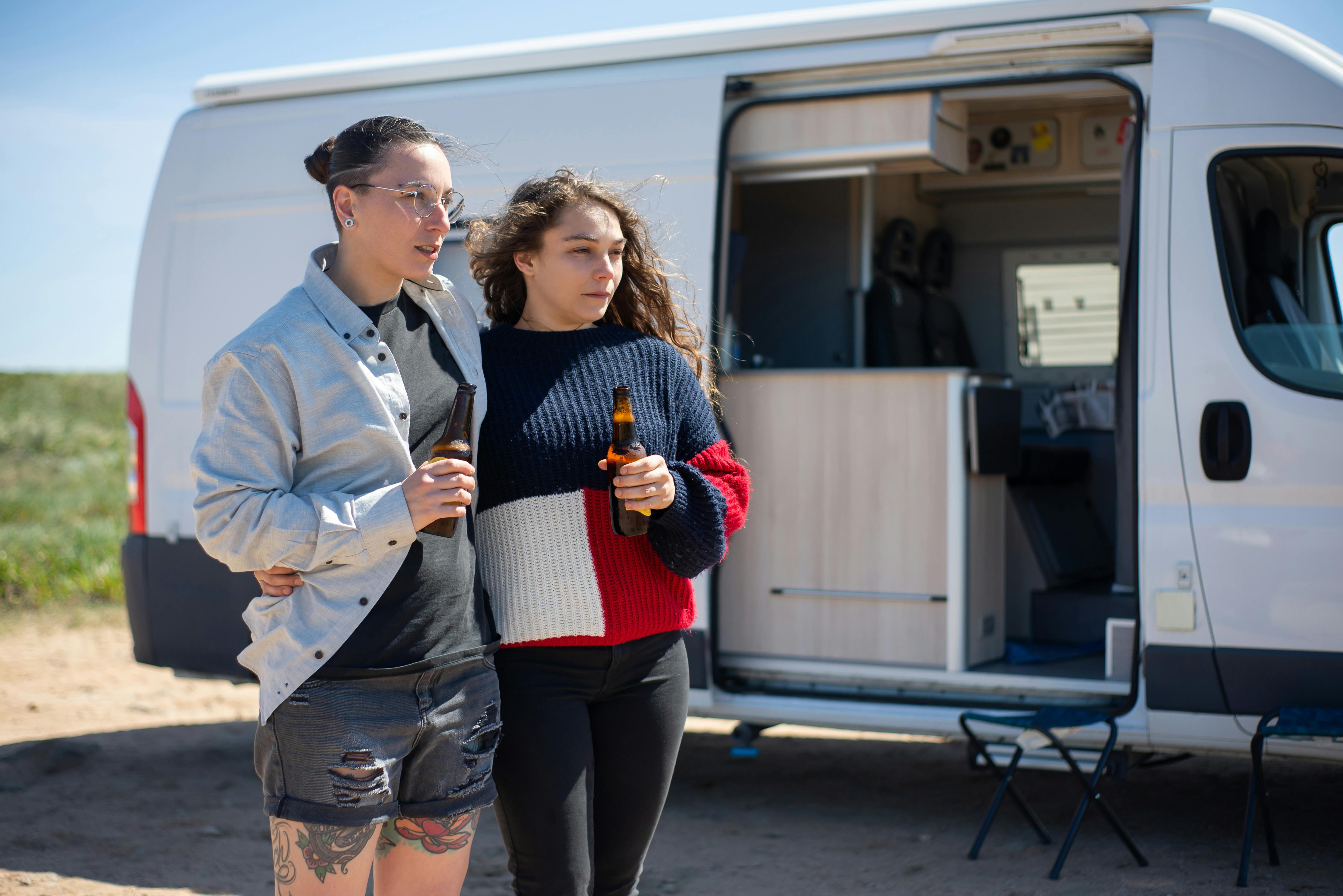 women holding beer bottles while standing beside a motorhome