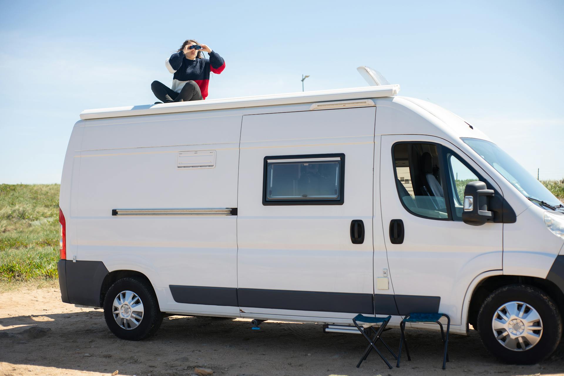 A Woman Using Binoculars while Sitting on Top of a Motorhome