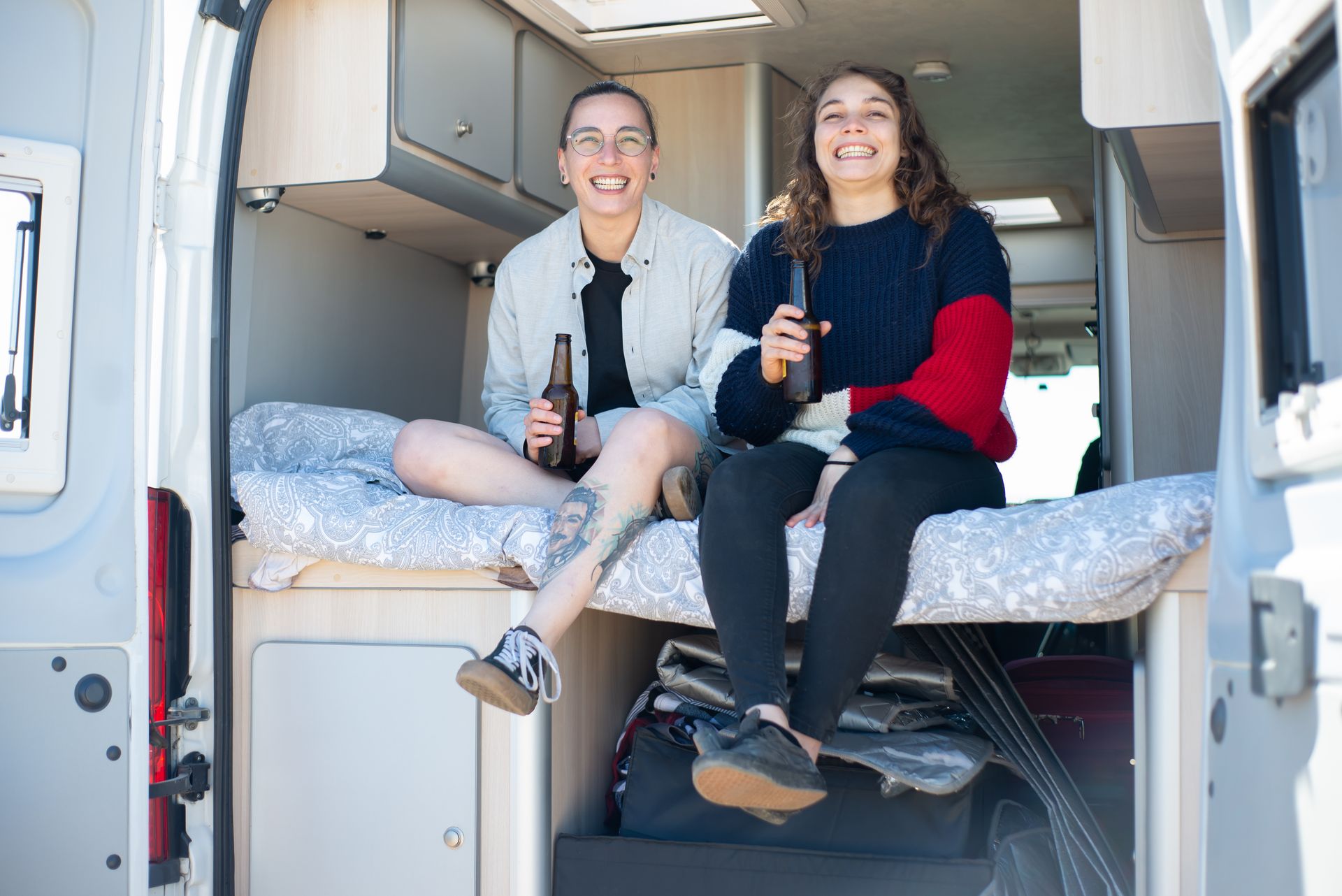 A Couple Holding Beer Bottles While Sitting in an RV