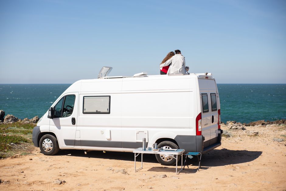 Romantic couple sitting on camper van roof enjoying ocean view
