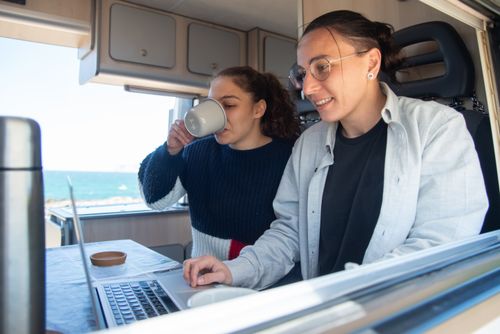 Free A joyful couple works on a laptop in a cozy camper van with ocean views. Stock Photo