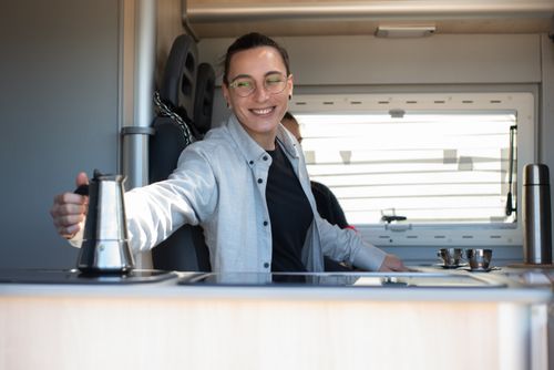 Free Caucasian person smiling while preparing coffee inside an RV kitchen in Portugal. Stock Photo