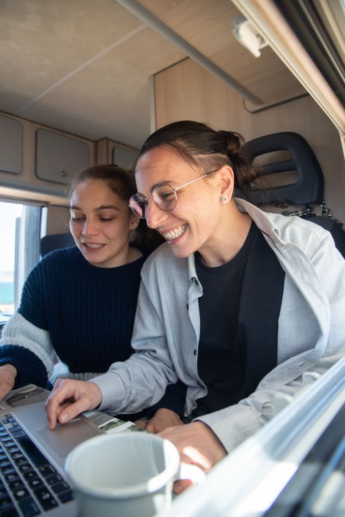 Free Lesbian couple enjoying a day working together inside a cozy camper van in Portugal, smiling and relaxed. Stock Photo