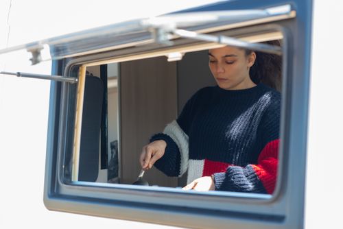 Free Woman preparing food inside camper van, showcasing mobile living lifestyle. Stock Photo