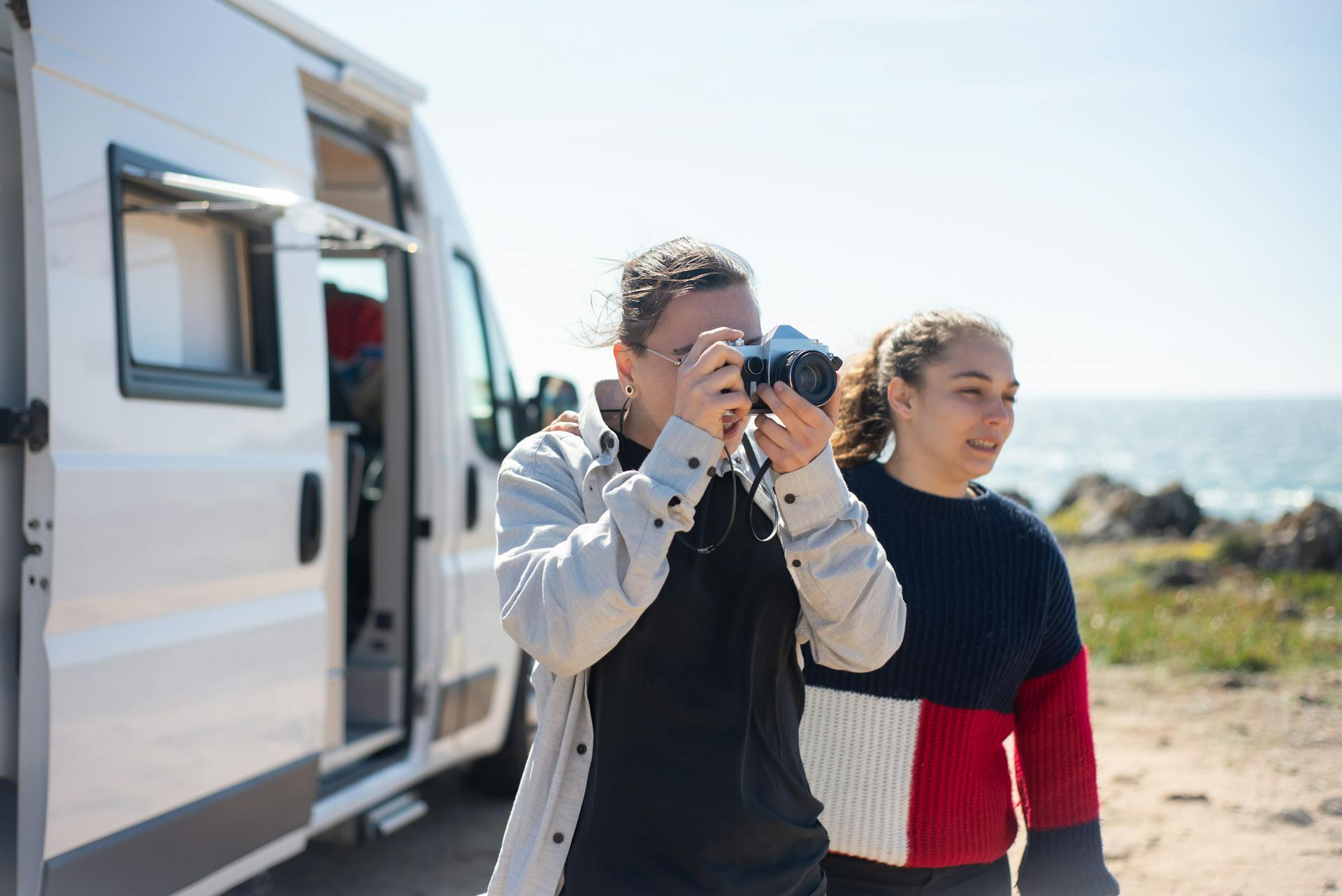 Two women enjoying a coastal adventure in Portugal with a camera and camper van.
