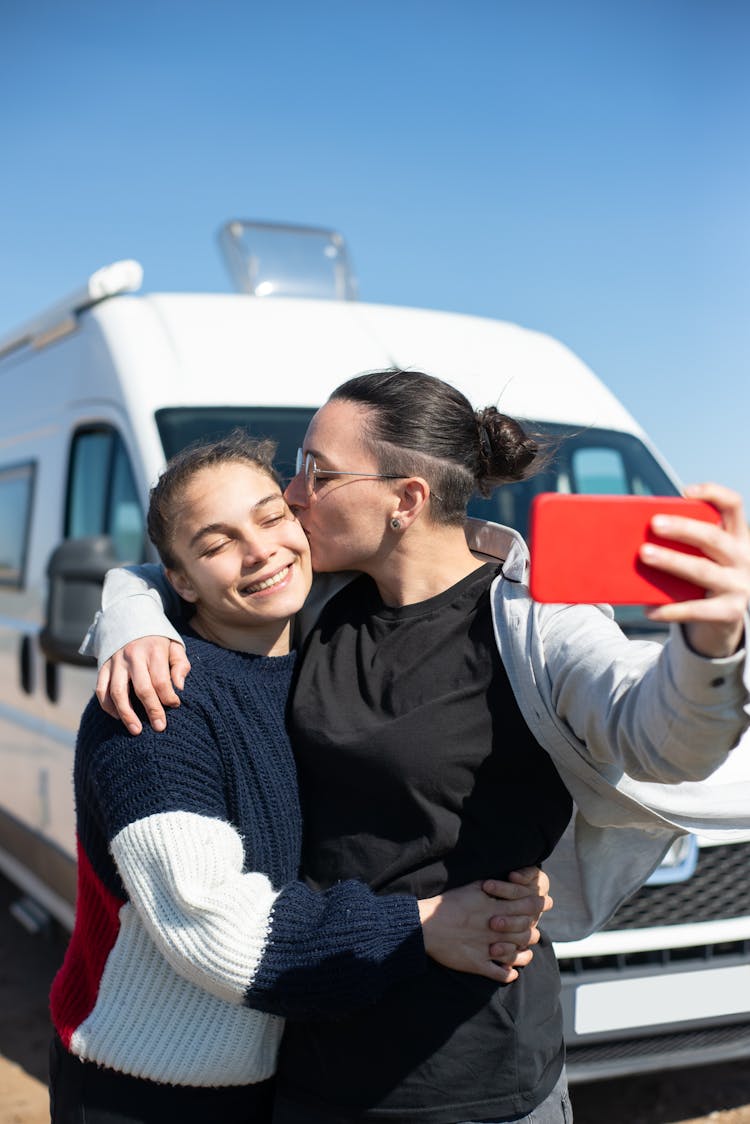 Photo Of A Woman Kissing Another Woman While Taking A Picture On The Phone