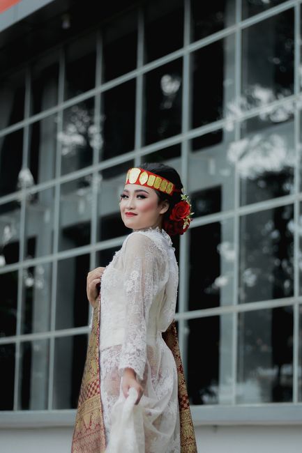 A woman in traditional attire poses gracefully against a modern glass building backdrop.