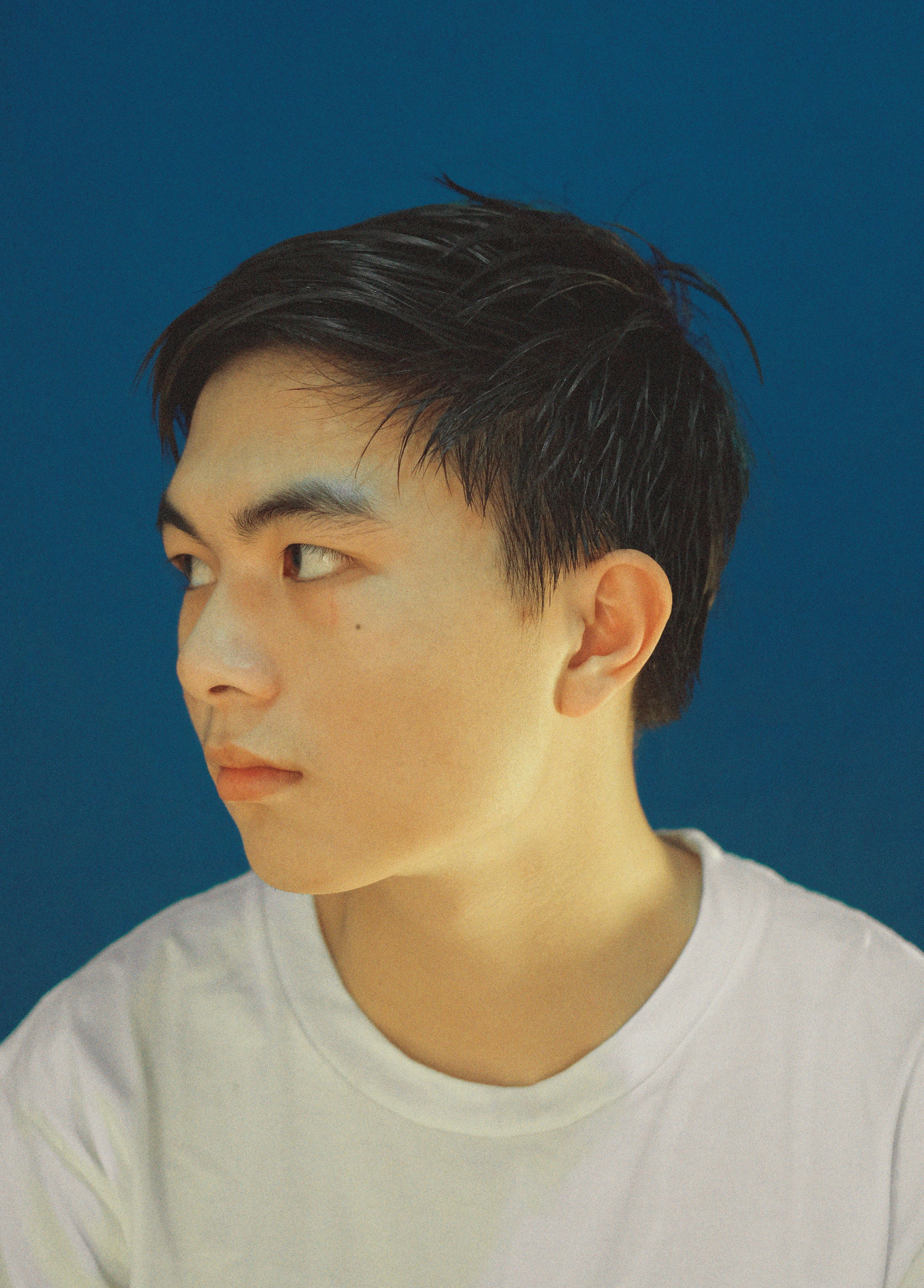 Serious portrait of an East Asian teenage boy against a blue background in Vietnam.