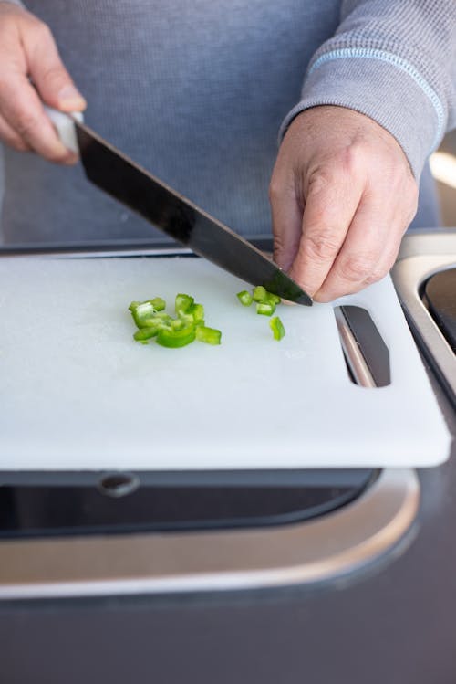 Person Holding Green Vegetable on White Chopping Board