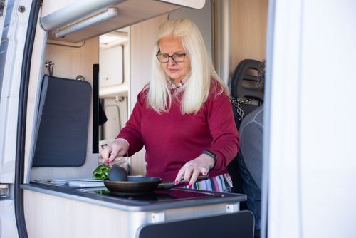 Free Senior woman preparing a meal in a motorhome kitchen, embracing travel and lifestyle freedom. Stock Photo