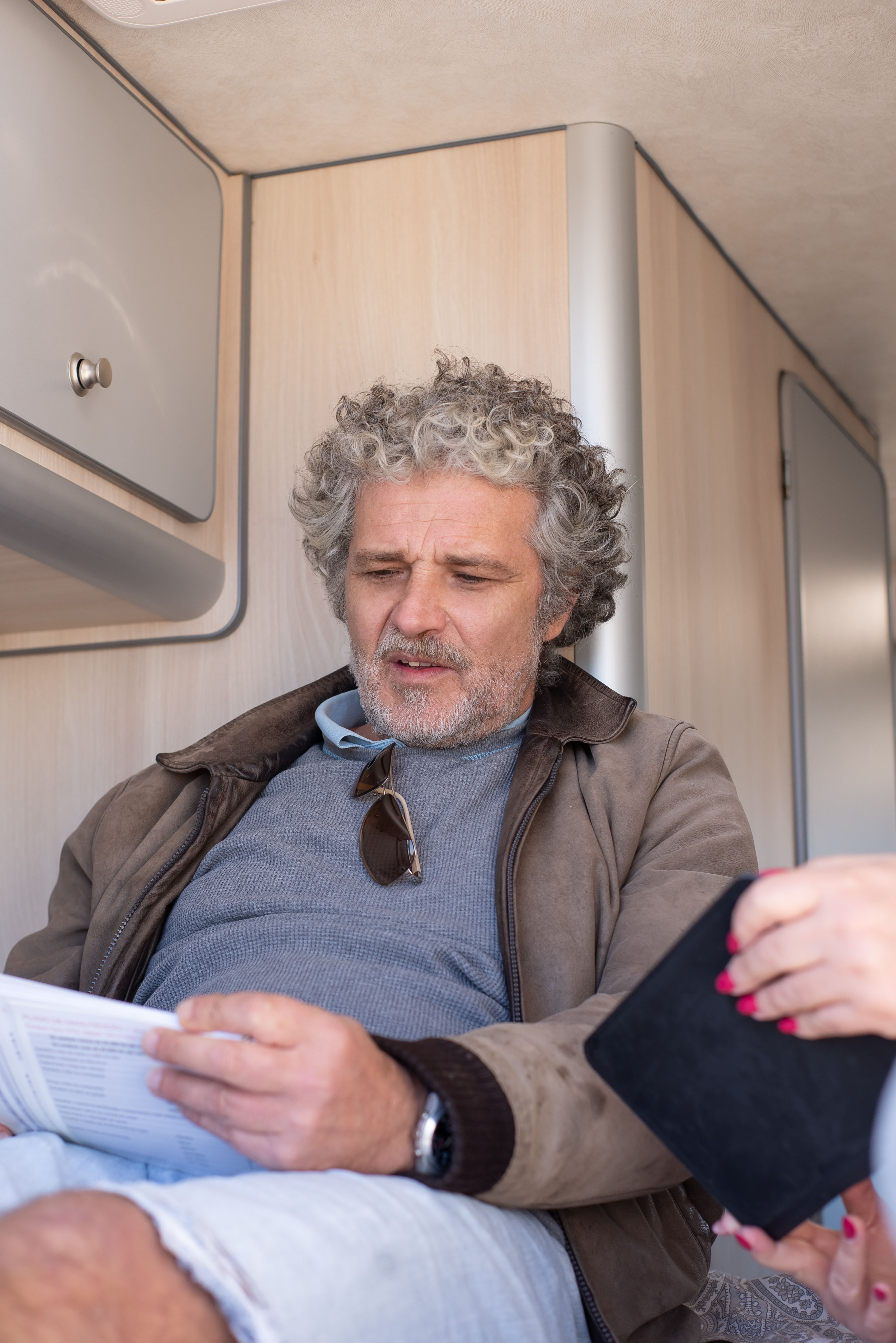 A senior man reads inside a camper van, holding a document.